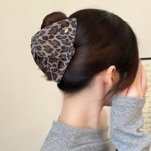 Leopard print fabric hair claw clip with gold label shown in a messy bun hairstyle