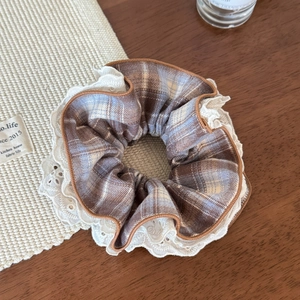 Detail view of plaid scrunchie with white lace embroidery on a vintage wood surface