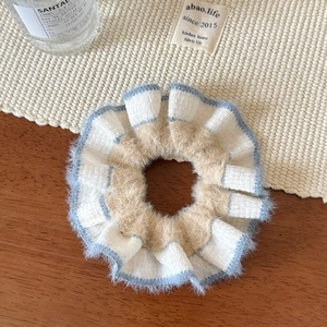 Close-up of hand-woven beige and blue plush scrunchie on a rustic wooden background