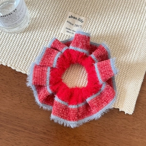 Close-up of a handmade red knitted scrunchie with grey fuzzy trim on a woven texture mat