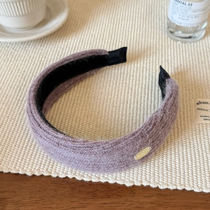 Detail of purple knitted headband with soft fuzzy texture and small gold metal emblem