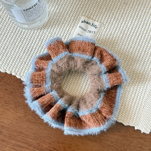 Detail of plush brown scrunchie with blue trim and white fabric label on woven mat