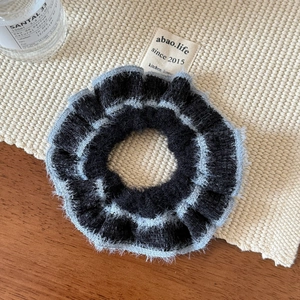 Detail of hand-knitted black scrunchie with soft light blue faux fur edges on a beige mat