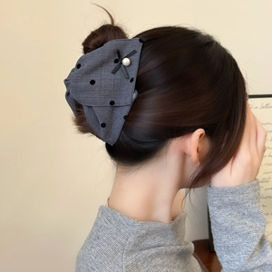 Detailed view of a grey polka dot bow hair claw with a pearl accent on a bun hairstyle