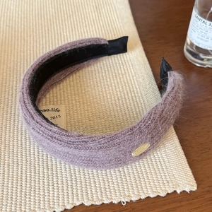 Close-up of fluffy mauve knit headband featuring golden metal tag and luxury texture