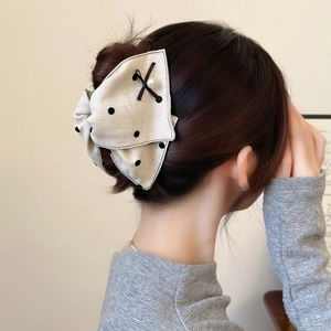 Polka dot bow hair clip with white pearl detail worn on a high bun hairstyle