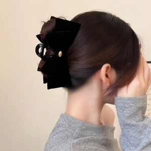 Elegant black velvet bow hair claw with gold emblem shown in hair from a side view