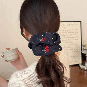 Navy blue polka dot scrunchie with red cherry embroidery on brunette hair in cozy setting