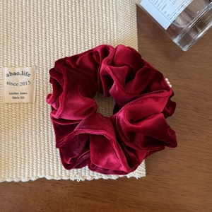 Texture détaillée du chouchou en velours bordeaux avec des plis élégants sur fond tissu