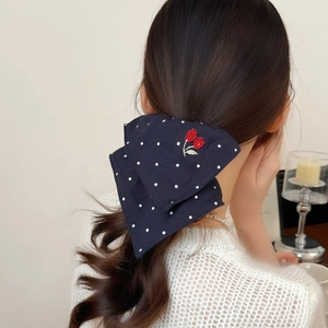 Polka dot navy scrunchie with red cherry embroidery worn on wavy brown hair