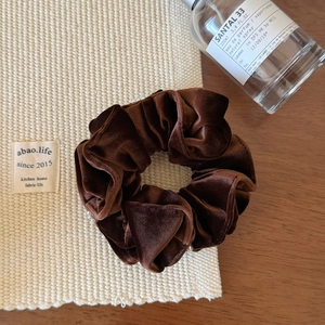 Détail d'un chouchou en velours marron foncé avec perles blanches sur tissu texturé