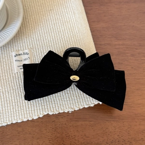 Detail view of a black velvet bow hair claw with a gold Wings metal badge for women