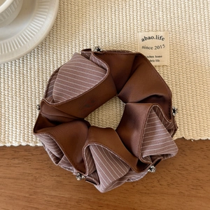 Close-up of brown striped silk scrunchie with silver beaded edges on beige woven mat