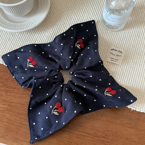 Detail of navy blue polka dot scrunchie with red cherry embroidery on fabric