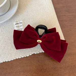 Detailed close-up of a burgundy velvet bow hair claw with elegant golden metal logo piece