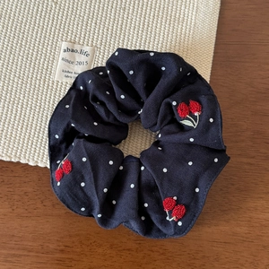 Close-up of retro black fabric scrunchie with white polka dots and red cherry embroidery