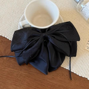 Elegant black satin bow hair clip with flowing ribbons on a rustic aesthetic wooden table