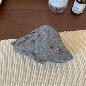Détail de la pince à cheveux grise tricotée avec broderie cerise sur tapis tissé
