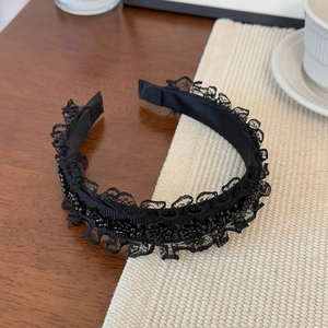 Close-up of black lace headband with elegant bead embellishments on a woven mat