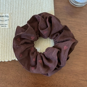 Detail of coffee brown scrunchie with pink heart patterns on a rustic woven background