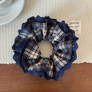Close-up of dark blue lace-trimmed plaid scrunchie hair tie on a rustic background