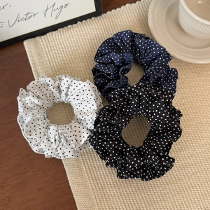 Three French style polka dot fabric scrunchies in white, navy and black on a woven mat