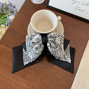 Close-up of black and white paisley bow hair claw clip with silk layers on wood surface