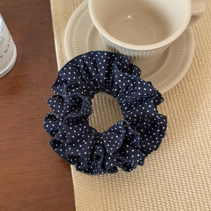 Navy blue polka dot scrunchie on beige woven mat with decorative aesthetic lifestyle props