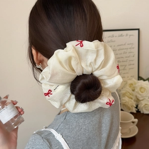 White organza scrunchie with red bow embroidery on elegant bun in cozy setting