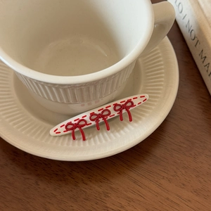 Close-up of red bow polka dot hair clip on a white ceramic saucer with vintage background