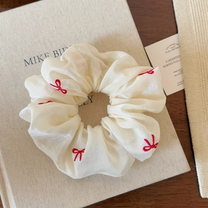 Macro detail of cream chiffon scrunchie with red embroidered bows on fabric book