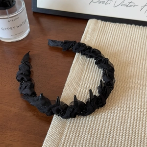 Détail d'un serre-tête noir ondulé avec plis en mesh, perles et dents de préhension