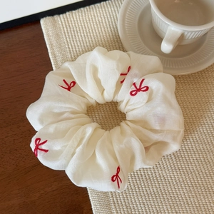Close-up of cream scrunchie with red bow embroidery on elegant pleated chiffon fabric