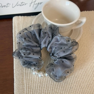 Close-up of a grey polka dot organza scrunchie with white pearl accents on a table