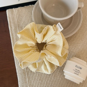 Detail of yellow and white striped fabric scrunchie with a handmade tag in a lifestyle setting