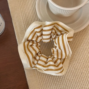 Detail of yellow striped fabric scrunchie on beige textured mat with a coffee cup