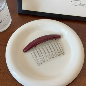 Détail d'un peigne à cheveux bordeaux à 12 dents présenté sur un plateau en céramique