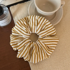 Detail of yellow and white striped fabric scrunchie on a rustic table with accessories