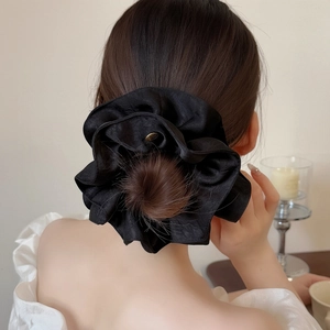 Elegant large black silk-like scrunchie with gold label shown on high bun hairstyle