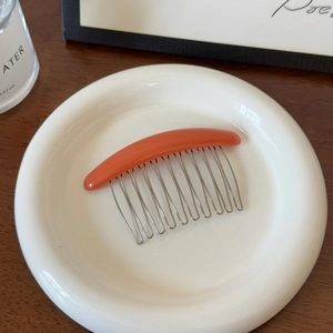 Détail d'un peigne à cheveux orange à 10 dents en métal sur une assiette en céramique