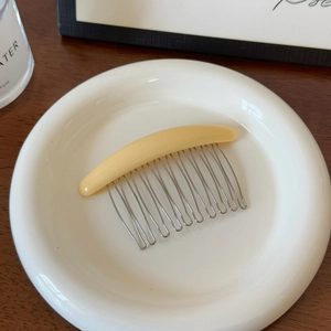 Gros plan d'un peigne à cheveux jaune crème avec douze dents en métal argenté sur plateau