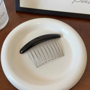 Détail montrant la barre noire élégante et les dents métalliques en U du peigne à cheveux