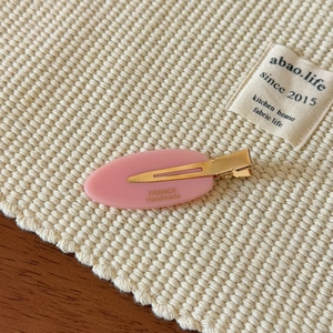 Close-up of pink leaf hair clip with gold metal duckbill clip on woven texture