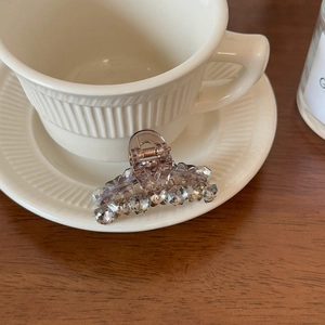 Close-up of translucent brown hair claw clip with crystal beads on a ceramic cup