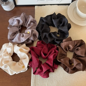 Detail view of five assorted silk scrunchies with gold logo tags on a wooden surface
