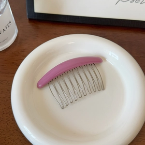 Détail d'un peigne à cheveux en résine violette avec dents en métal argenté sur une assiette