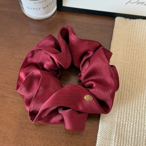 Macro shot of elegant burgundy silk scrunchie with golden oval metal brand tag on wood