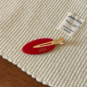 Close-up of a red leaf-shaped hair clip with gold metal spring clip and France handmade logo