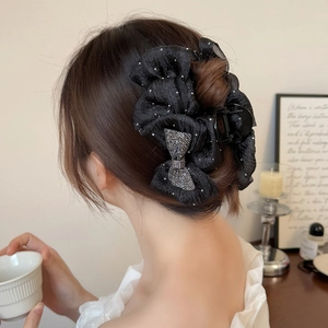 Detail view of a large black mesh bow hair claw clip with rhinestones worn by a model