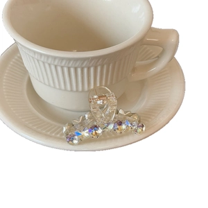 Elegant transparent hair claw clip with iridescent rhinestones on a coffee cup